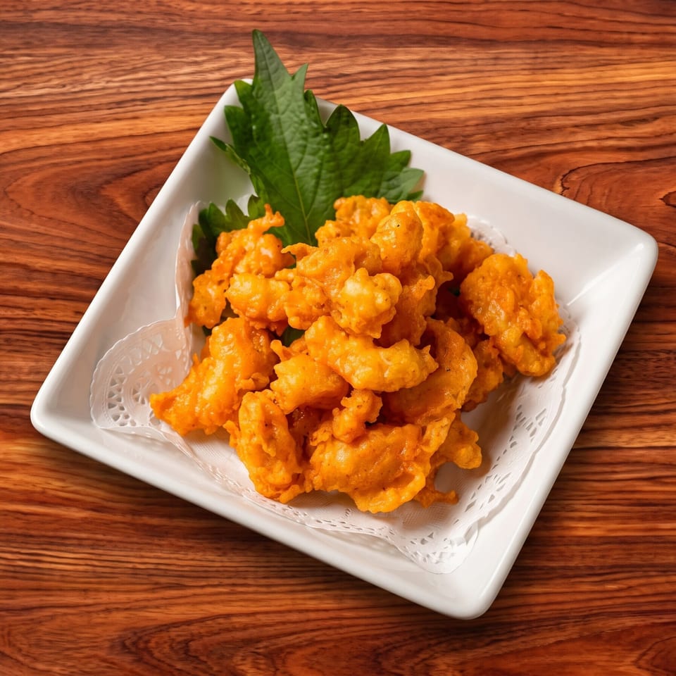Crispy orange fried chicken pieces on a white rectangular plate with green garnish on a wooden table.