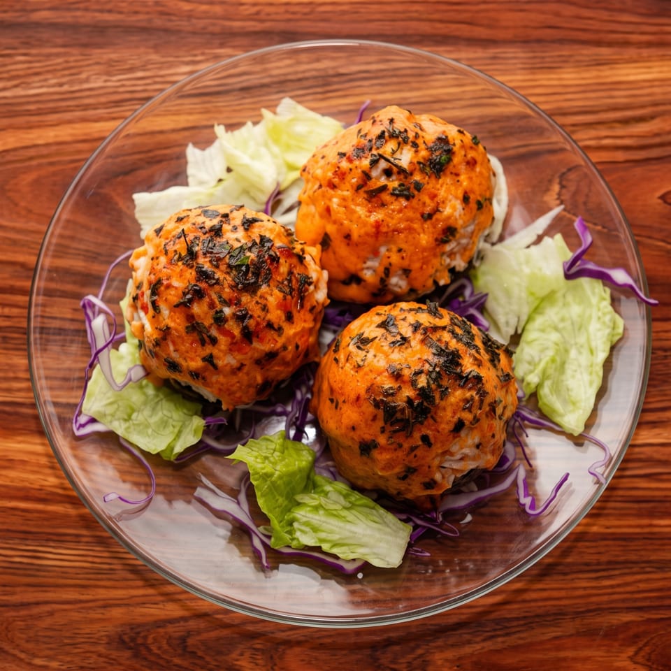 Three orange-colored, herb-crusted meatballs on a bed of lettuce and purple cabbage on a glass plate.